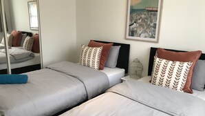 A hotel room with two beds, each with grey linens and brown patterned pillows. There is a large mirror on one wall and a painting above the bed. - Swale Corner (Wellingborough)