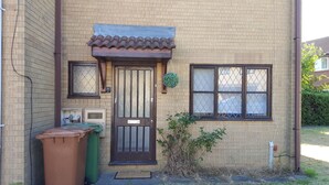 A two-story brick house with a brown door, two windows, and a small porch area. - Swale Corner (Wellingborough)