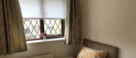 Un dormitorio con cama, un radiador, una ventana con cortinas, una mesita de noche y una lámpara.