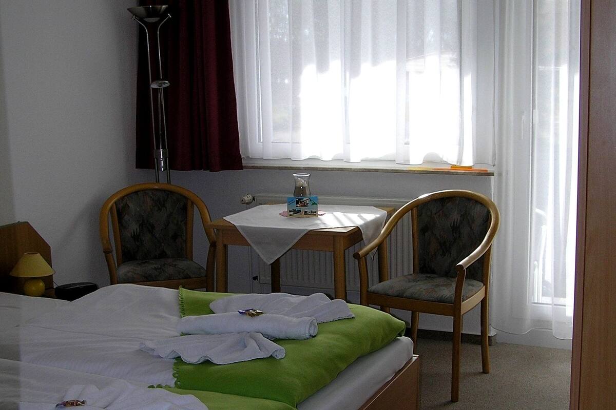 A hotel room with a bed, two chairs, a small table, and a window with curtains.