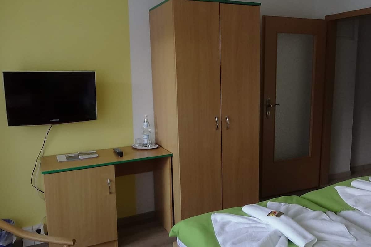 A hotel room with a bed, a desk, a television, and a wardrobe.