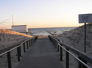 A wooden boardwalk leading to a beach with a lifeguard tower and a signpost. - Pension Dünenhaus (Zempin)