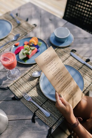 Una mesa servida con platos, cubiertos, una carta y una bebida.