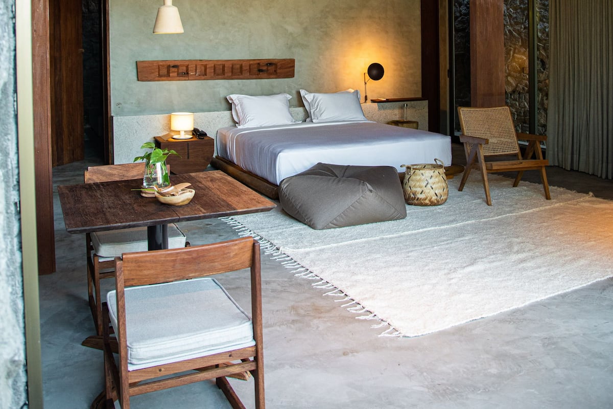 Une chambre moderne avec un plafond en bois, un lit recouvert de linge de maison blanc, une table de chevet avec une lampe et une chaise.