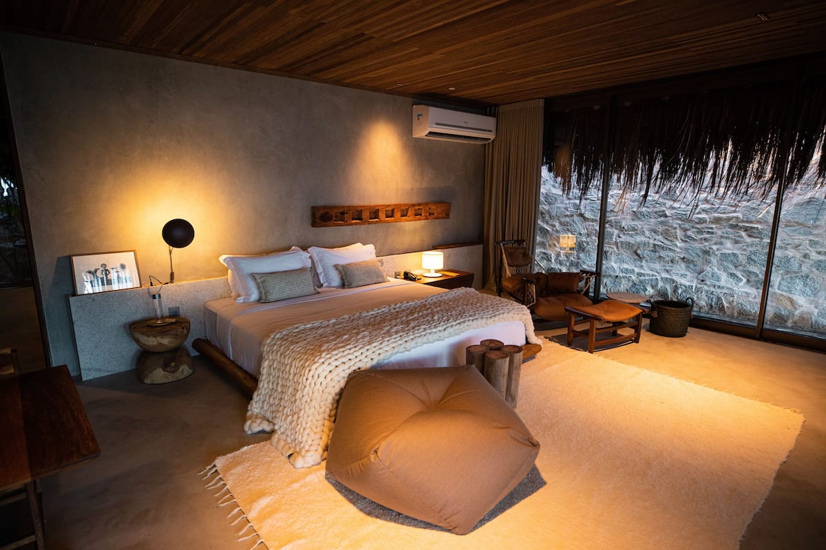 Une chambre avec un grand lit, une table de chevet, une chaise, une tête de lit en bois et une vue sur un paysage rocheux par la fenêtre.