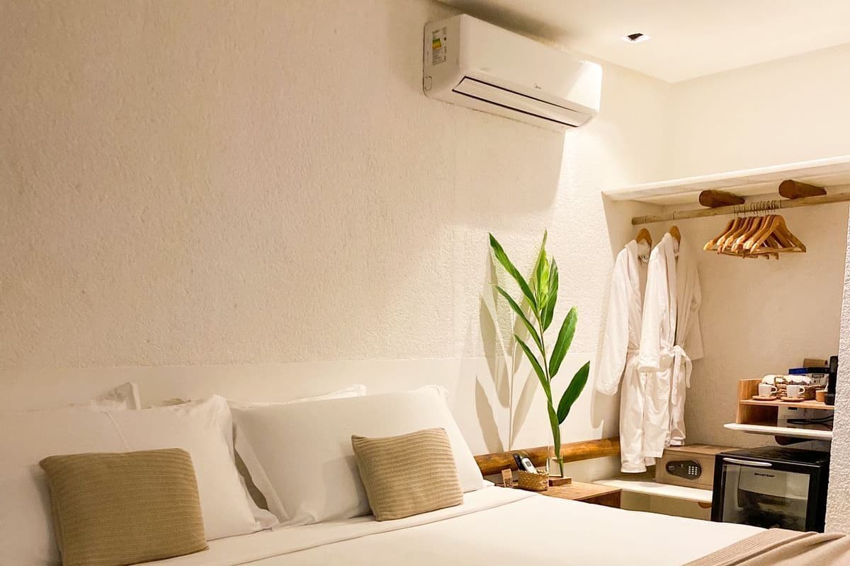 Une chambre d’hôtel avec un grand lit, une table de chevet avec une lampe, une plante et un porte-peignoir.