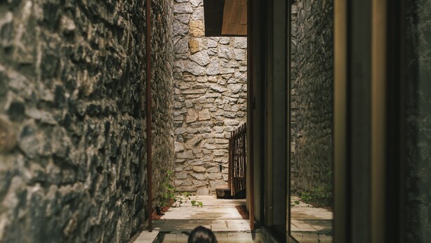 A person in a narrow water channel with stone walls and wooden beams, leading to a stone structure. - Paru Boutique Hotel (Passo de Camaragibe)
