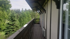 Una terraza de madera con barandilla, un área techada y vista a árboles.