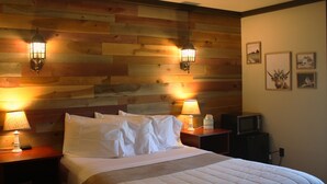 Un dormitorio con cabecera de madera, dos lámparas de noche, una cama con ropa blanca, una mesita de noche con un dispensador de pañuelos, un televisor y cuadros en la pared.