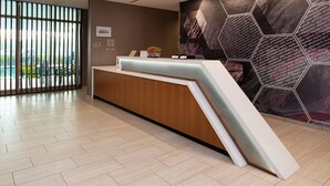 Een hotel receptie met een modern design, met een receptiebalie, een muur met honingraatpatroon en een uitzicht door grote ramen.
