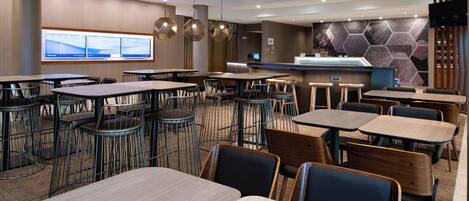 A modern restaurant with multiple seating areas, including round tables and booths, and a counter with a digital display.