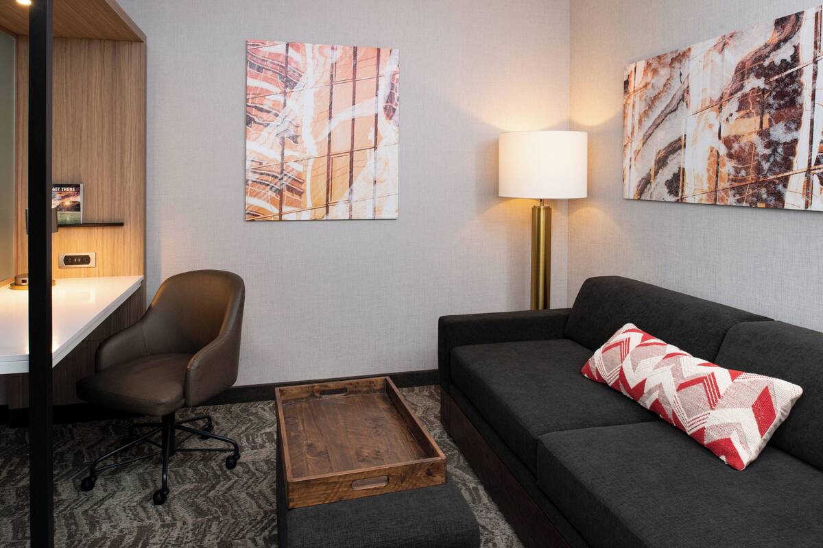 A modern living room with a grey sofa, a wooden coffee table, a black office chair, and two abstract paintings on the wall.