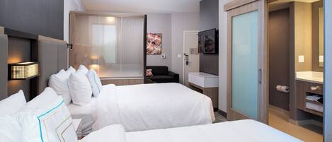 Une chambre d’hôtel avec deux lits, un bureau, une chaise, une télévision, un miroir et une armoire.