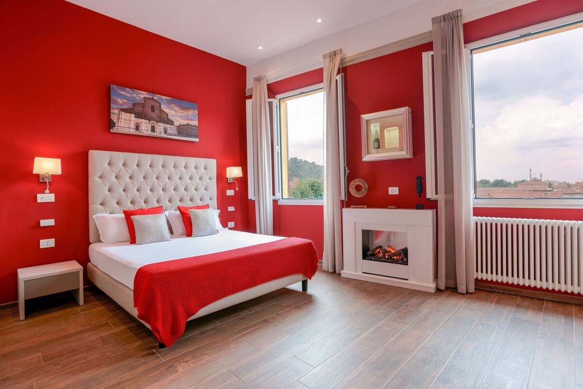 A bedroom with a large bed, a fireplace, and a view of a cityscape.