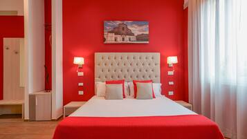 Quarto com parede vermelha, uma cama grande com roupa de cama branca e vermelha, duas luminárias de cabeceira e uma pintura de um edifício.