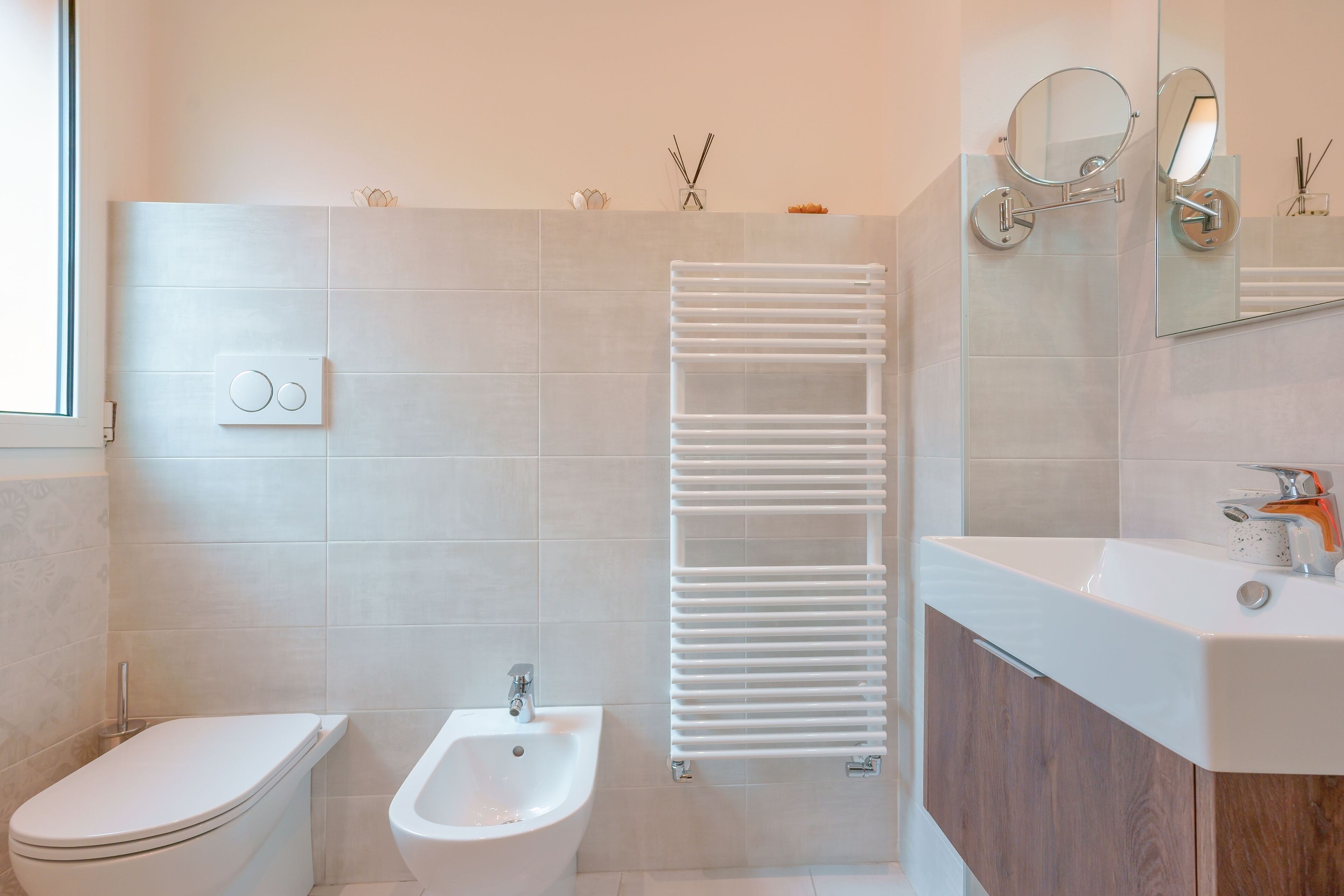 Et moderne badeværelse med toilet, bidet, hvidt håndklædestativ og et spejl over vasken.