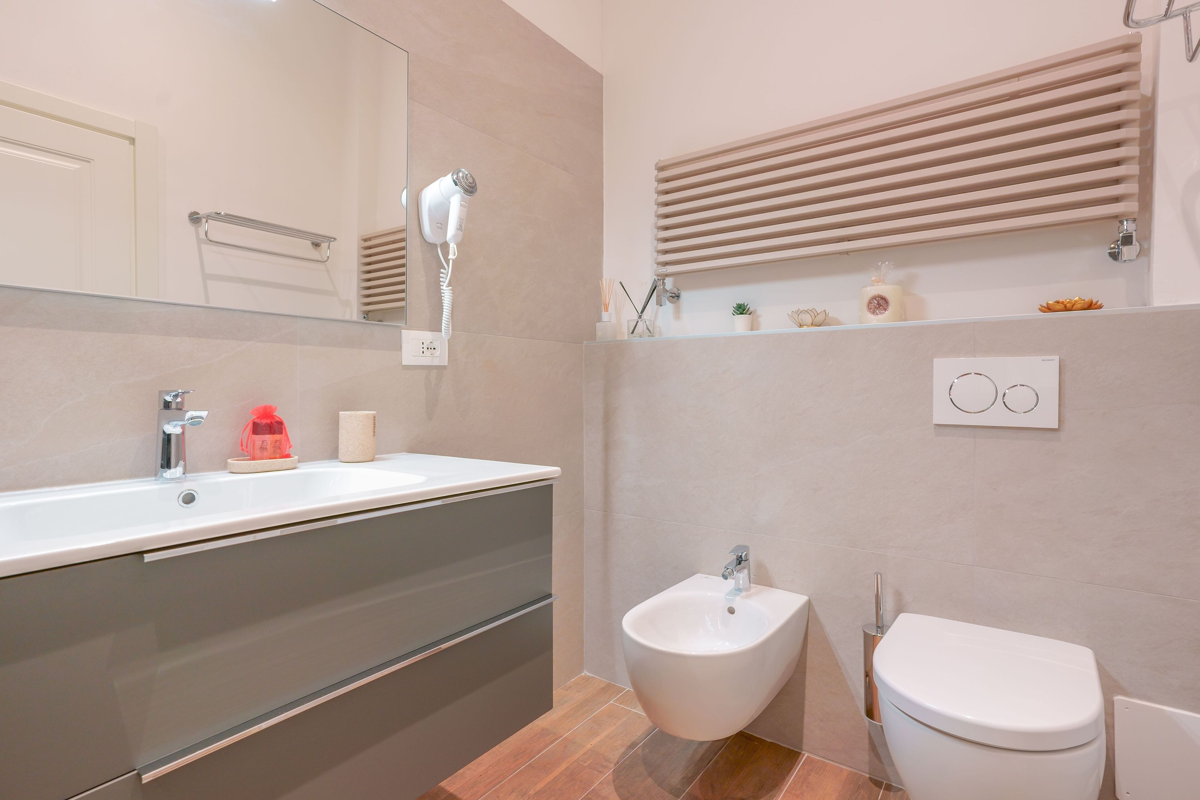 A modern bathroom with a large mirror, a bidet, a toilet, and a vanity with a sink.