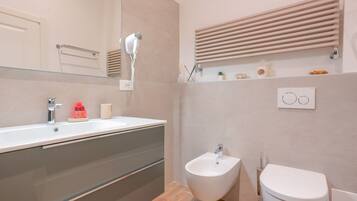A modern bathroom with a large mirror, a bidet, a toilet, and a vanity with a sink.