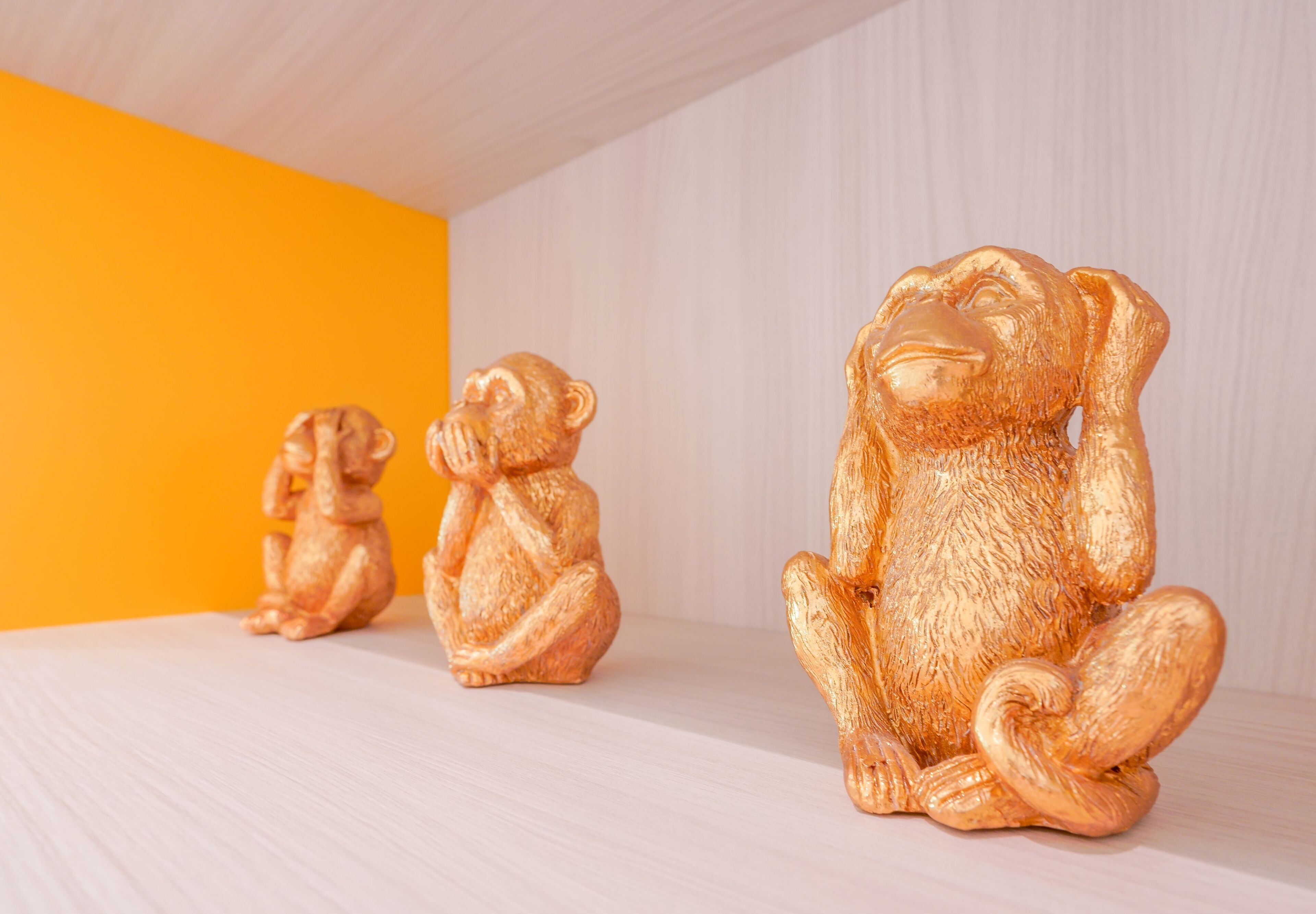 Tre gyllene Buddha-statyetter står på en hylla mot en bakgrund i vitt och orange.