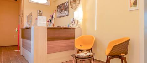 A reception area with a wooden reception desk, two chairs, a clock, and a framed picture on the wall.