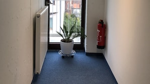 A hallway with a potted plant, a fire extinguisher, and an exit sign. - Hotel Mirabell (Erlangen)