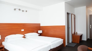 A hotel room with a large bed, a wooden headboard, a desk, and a chair. - Hotel Mirabell (Erlangen)