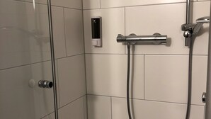 A modern shower with a handheld showerhead, a wall-mounted control panel, and a glass door. - Hotel Mirabell (Erlangen)