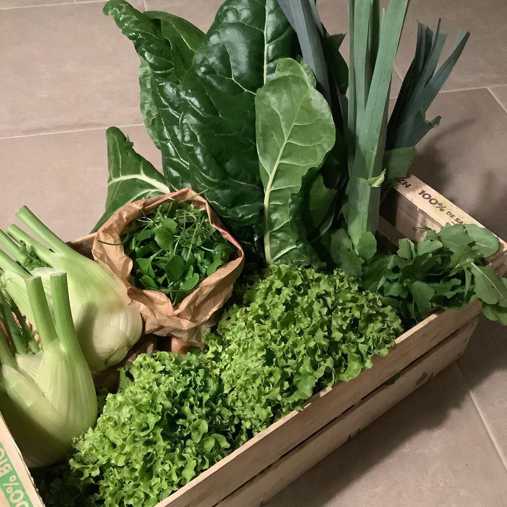Una caja de madera llena de diversas verduras y hojas verdes.