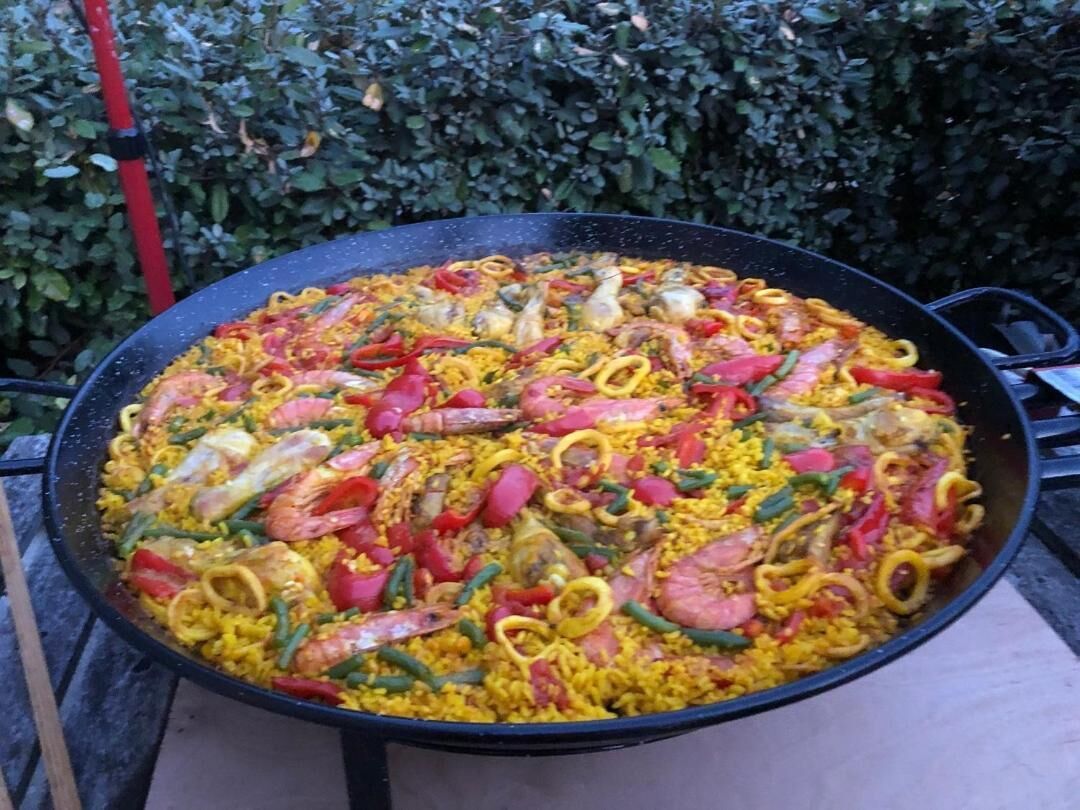 A large, round, black pan filled with a colorful seafood paella.