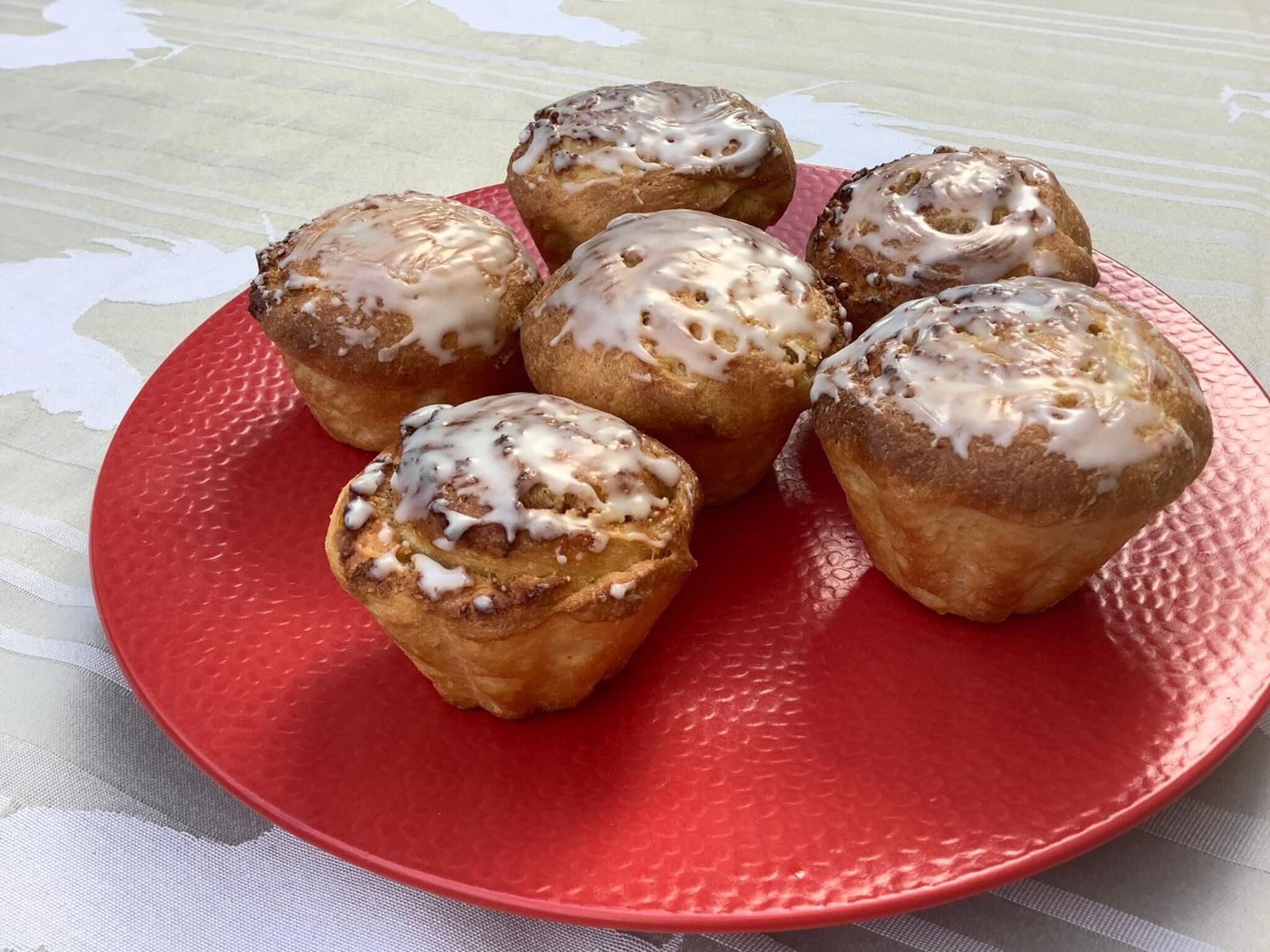 A plate of cinnamon rolls with icing on a red plate.