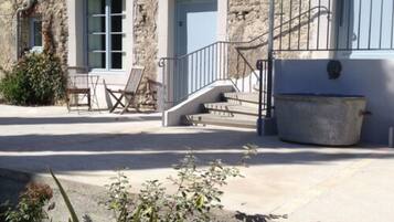A stone building with two windows and a door, a staircase, outdoor seating, and a planter.