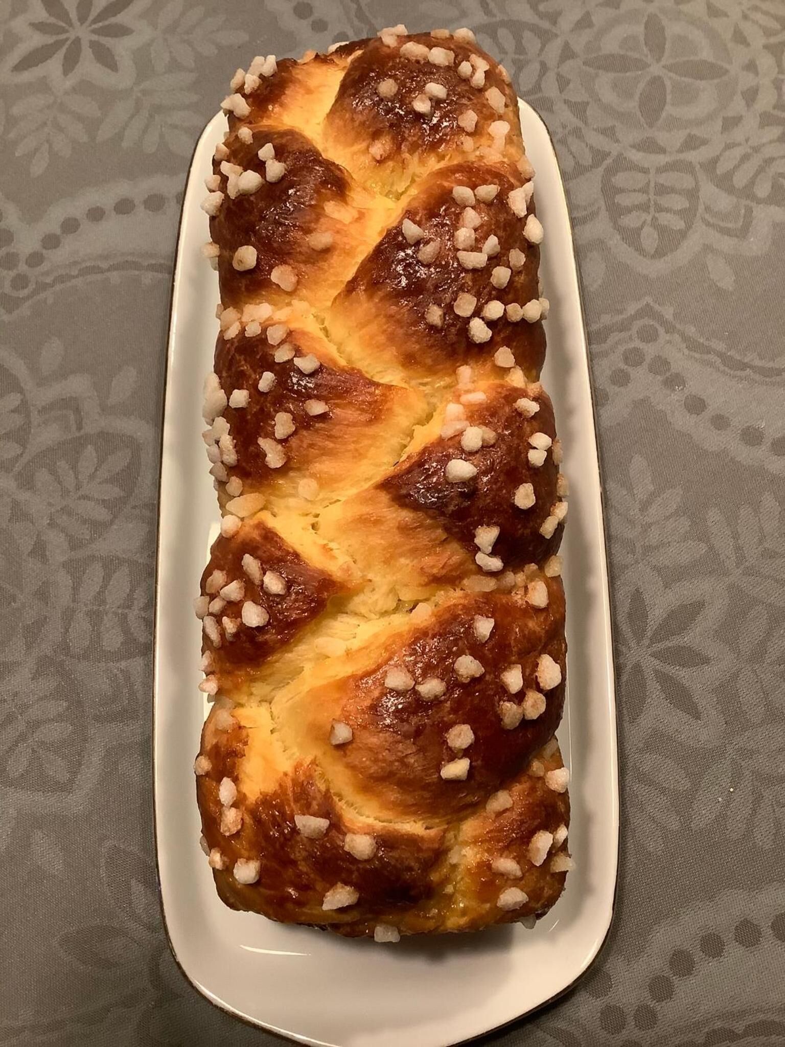A loaf of bread with a braided pattern and sugar crystals on top, placed on a white plate.