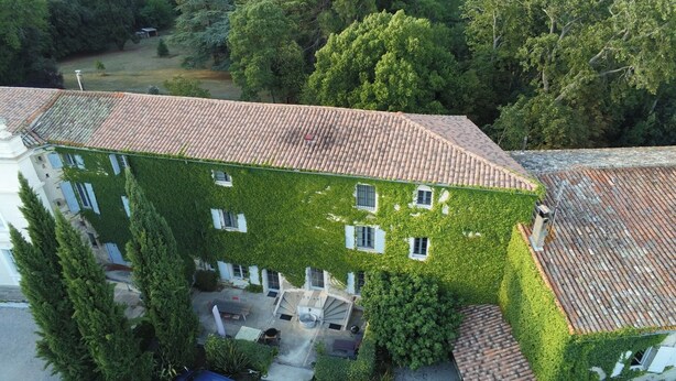 A multi-story building with a green ivy-covered exterior, a tiled roof, and a gravel driveway with a parked car. - Le Grenier Occitan (Gramazie)