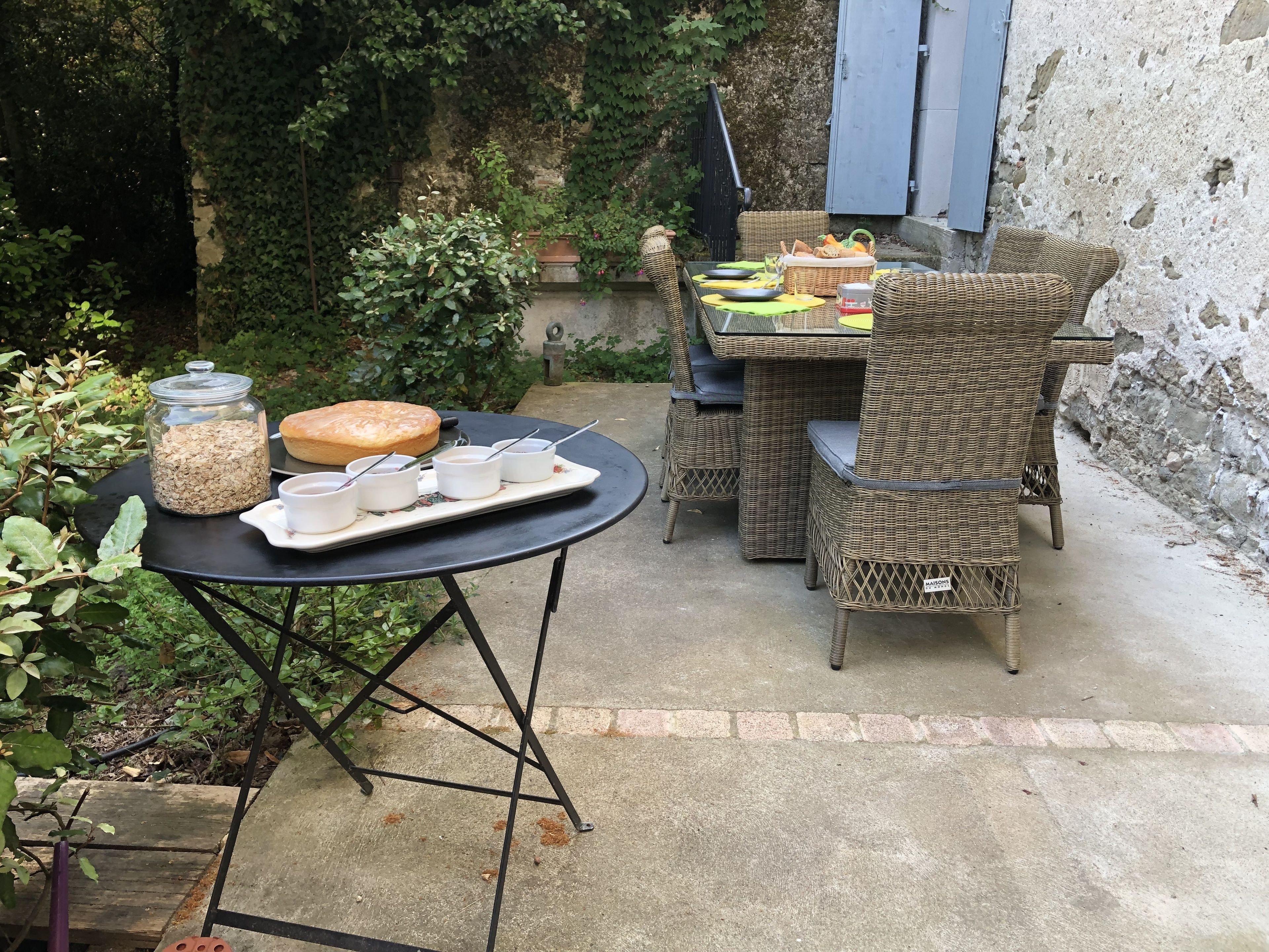 Una terrazza esterna con mobili in vimini, un tavolo con un vassoio di cibo e bevande, e un barattolo di avena.