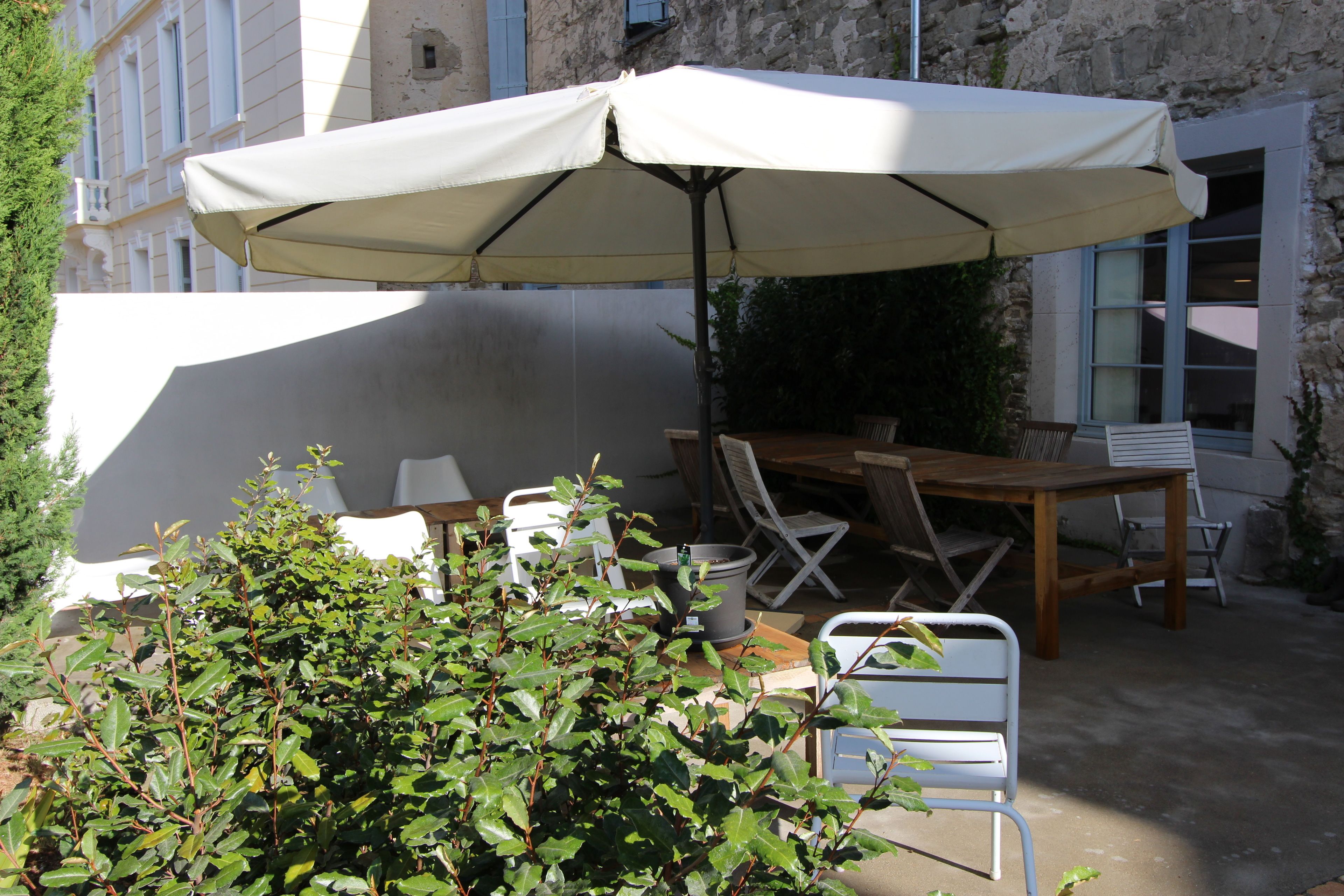 Un patio al aire libre con una mesa, sillas, un paraguas blanco y una planta en maceta.