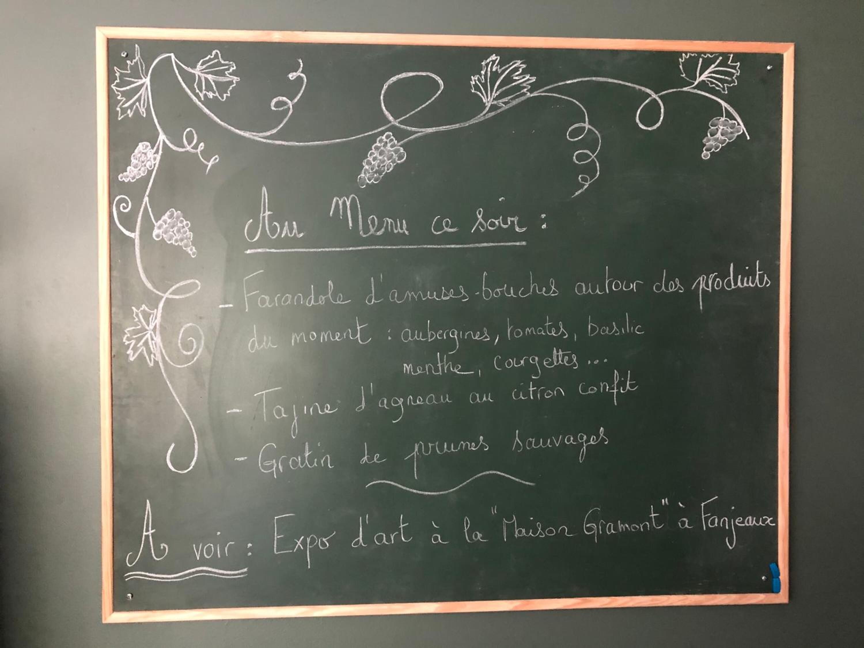Una pizarra con el menú, una lista de platos y una nota sobre una exposición de arte.
