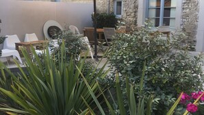 An outdoor seating area with a table and chairs, surrounded by plants and a large umbrella. - Le Grenier Occitan (Gramazie)
