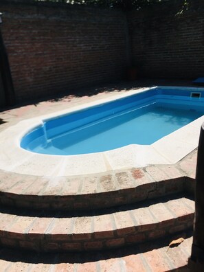Une piscine rectangulaire bordée de briques et dont le pourtour intérieur est blanc.