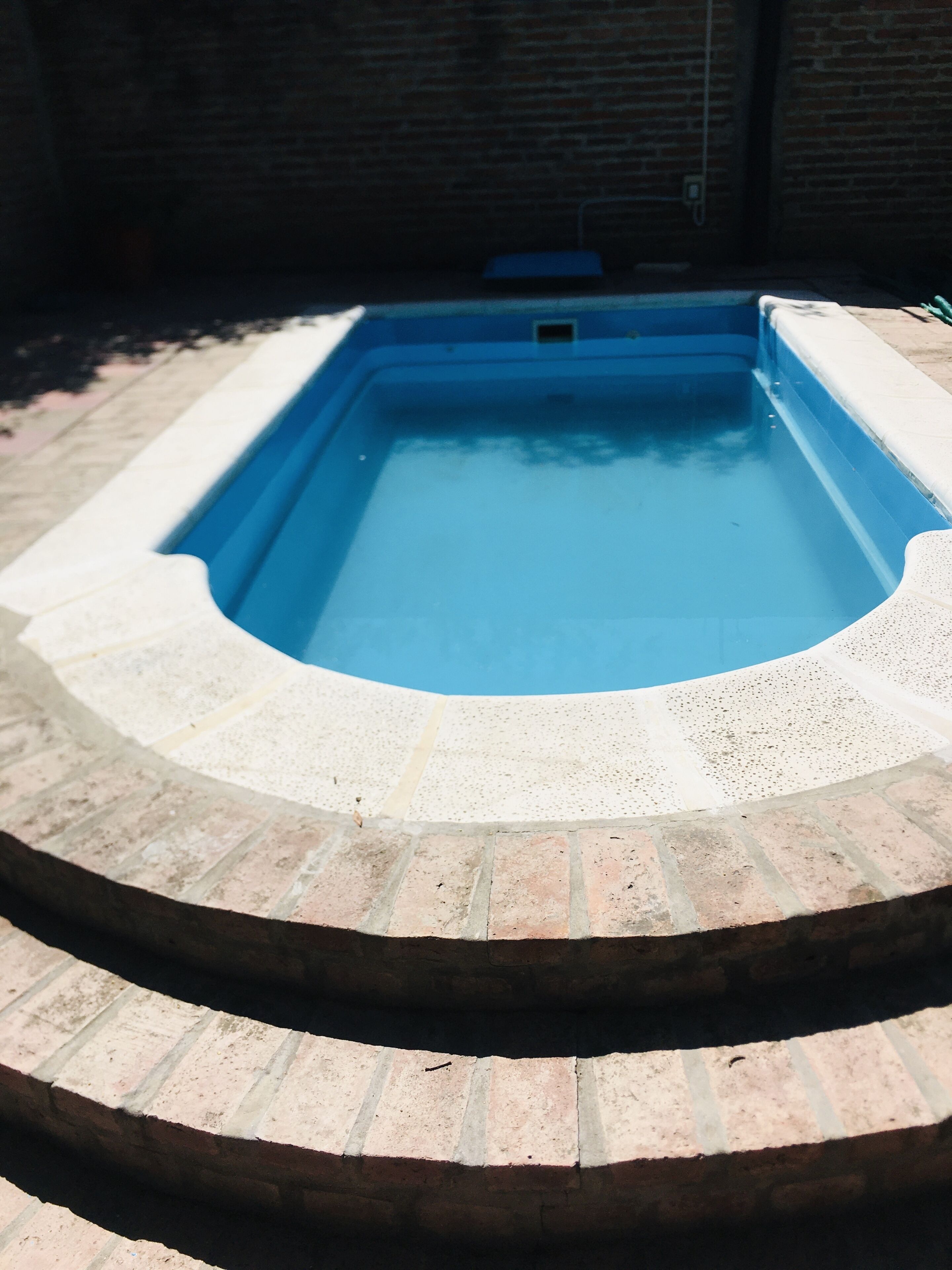 A rectangular swimming pool with a blue interior, surrounded by a brick border.