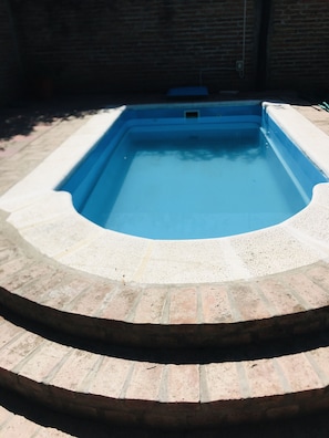 Ein rechteckiger Swimmingpool mit blauer Innenseite, umgeben von einer Ziegelkante.