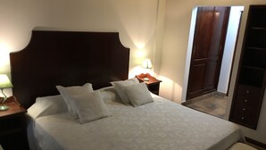 Ein ordentlich bezogenes Bett mit Holz-Kopfteil, ein Nachttisch mit Lampe und ein Schrank mit Spiegel.