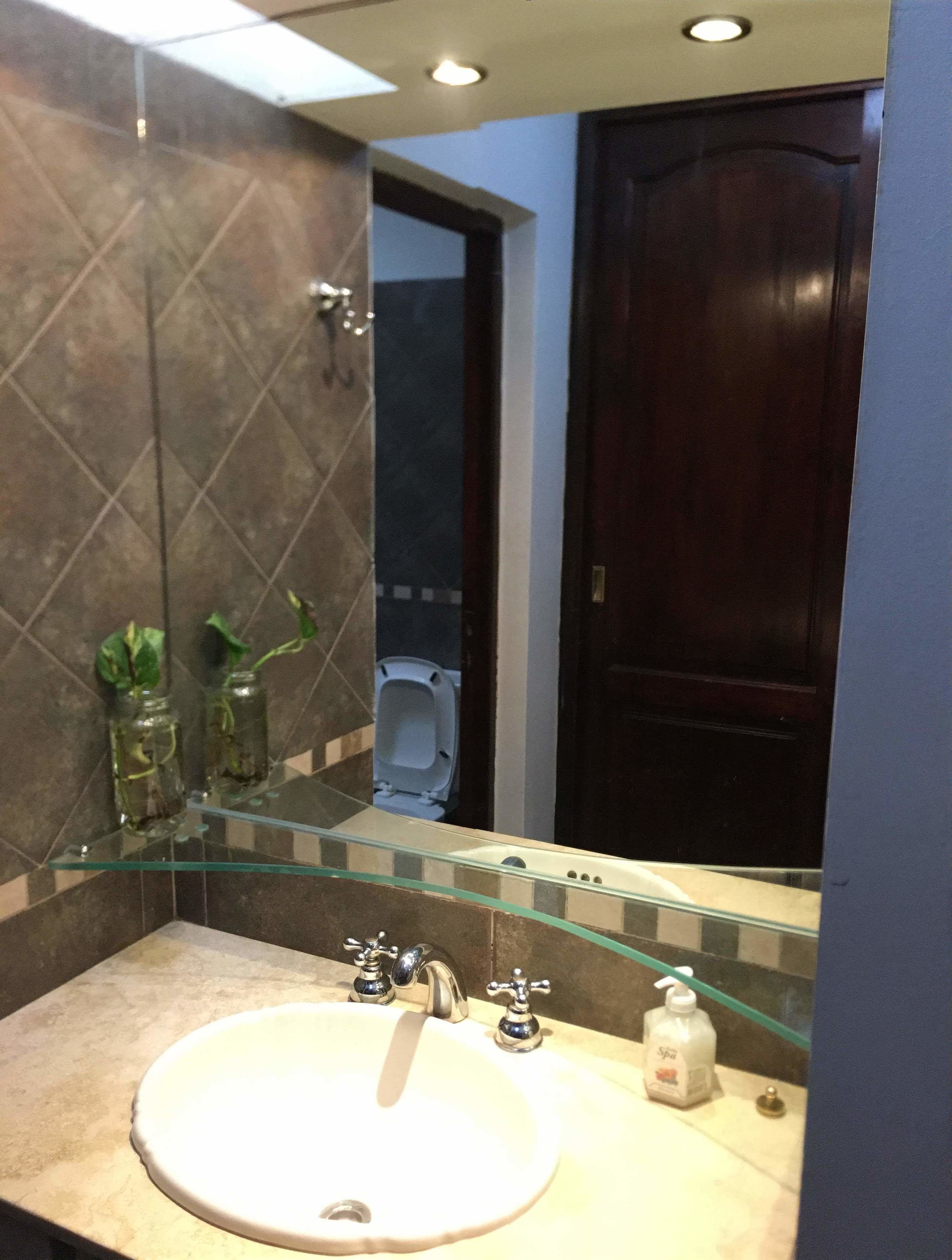 A bathroom with a round sink, two glass jars with plants, a glass shelf, a mirror, and a dark wooden door.