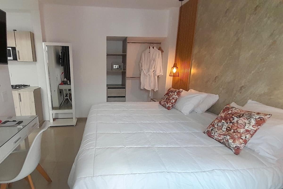 A bedroom with a large bed, a desk, a wardrobe, and a mirror.
