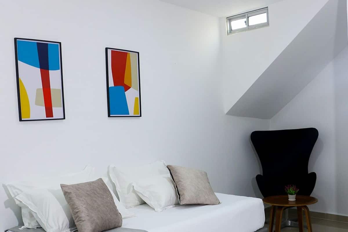 A modern bedroom with a sofa bed, a small table with a plant, and abstract art on the wall.