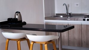 Una cocina con encimera negra, dos cuencos blancos sobre taburetes de madera, una tetera y un lavabo con grifo.