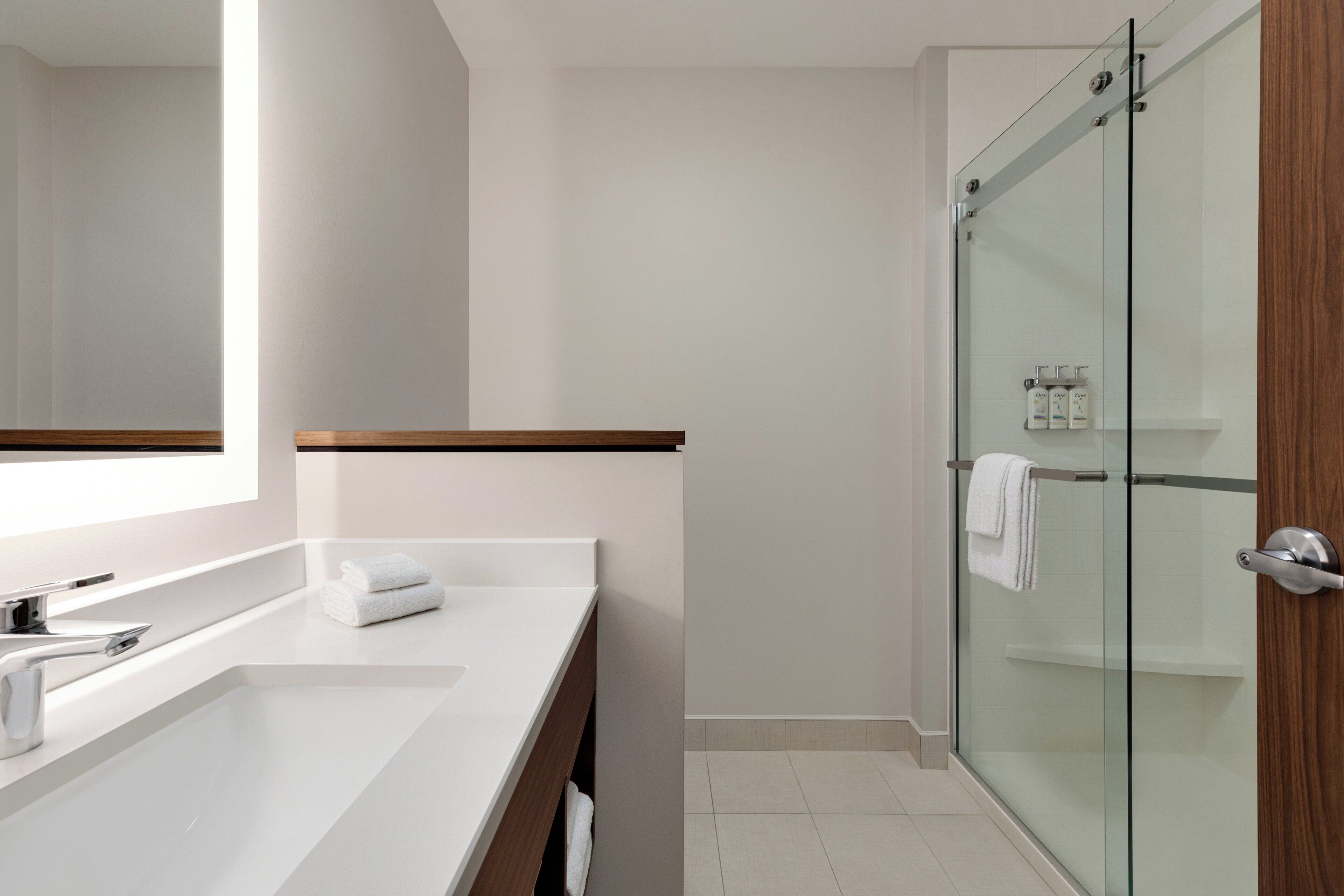 A modern bathroom with a large mirror, white sink, and a glass-enclosed shower area.