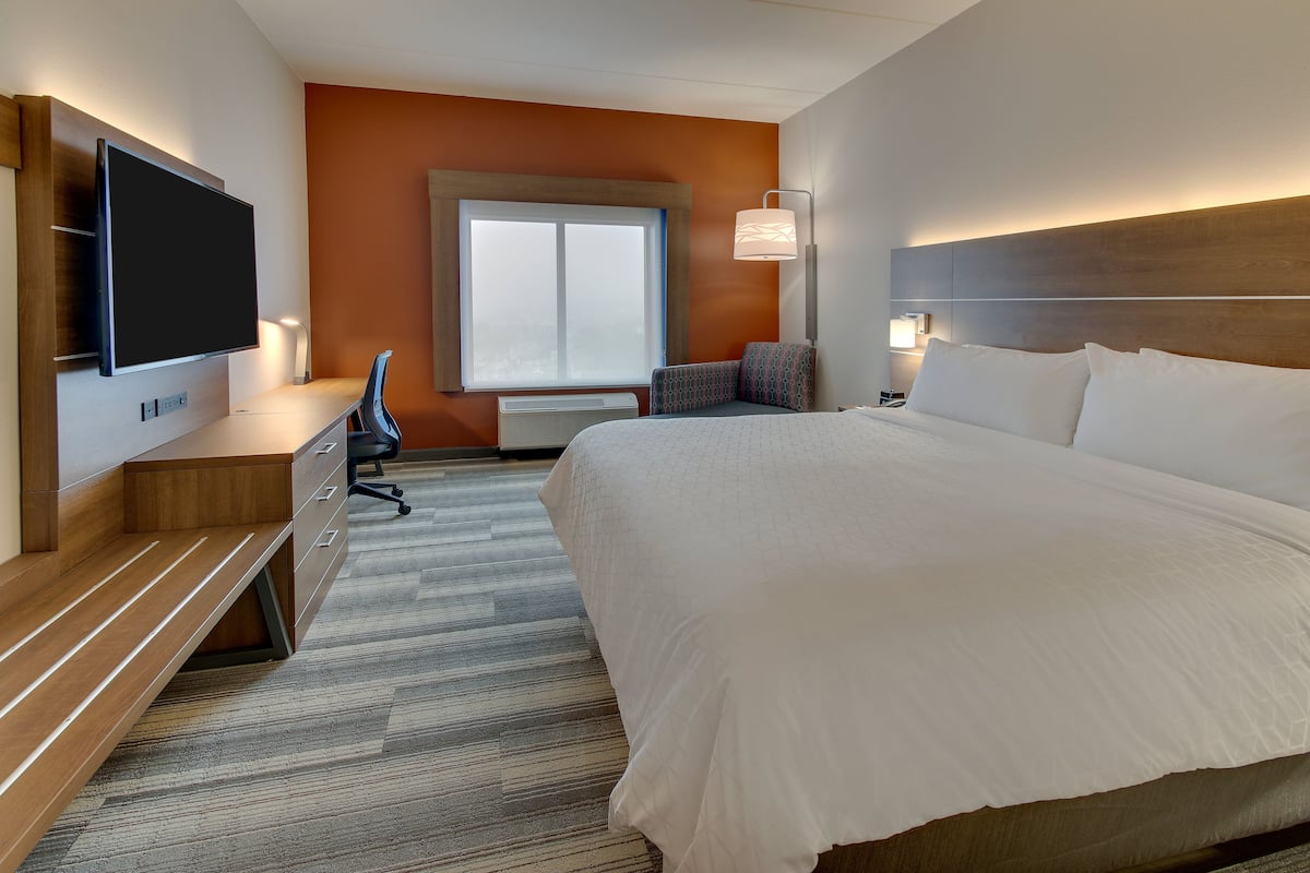 A hotel room with a large bed, a desk with a flat-screen TV, a chair, and a window with a view.