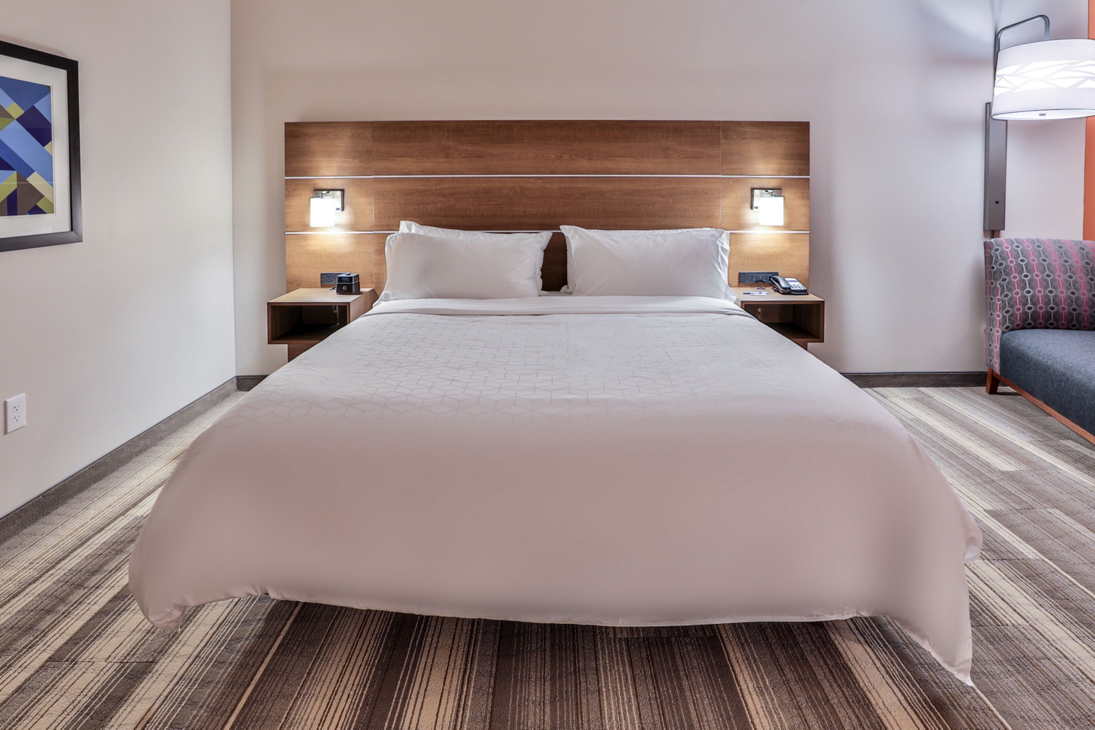 Habitación de hotel con una cama grande, dos mesitas de noche, una butaca y una lámpara de pared.