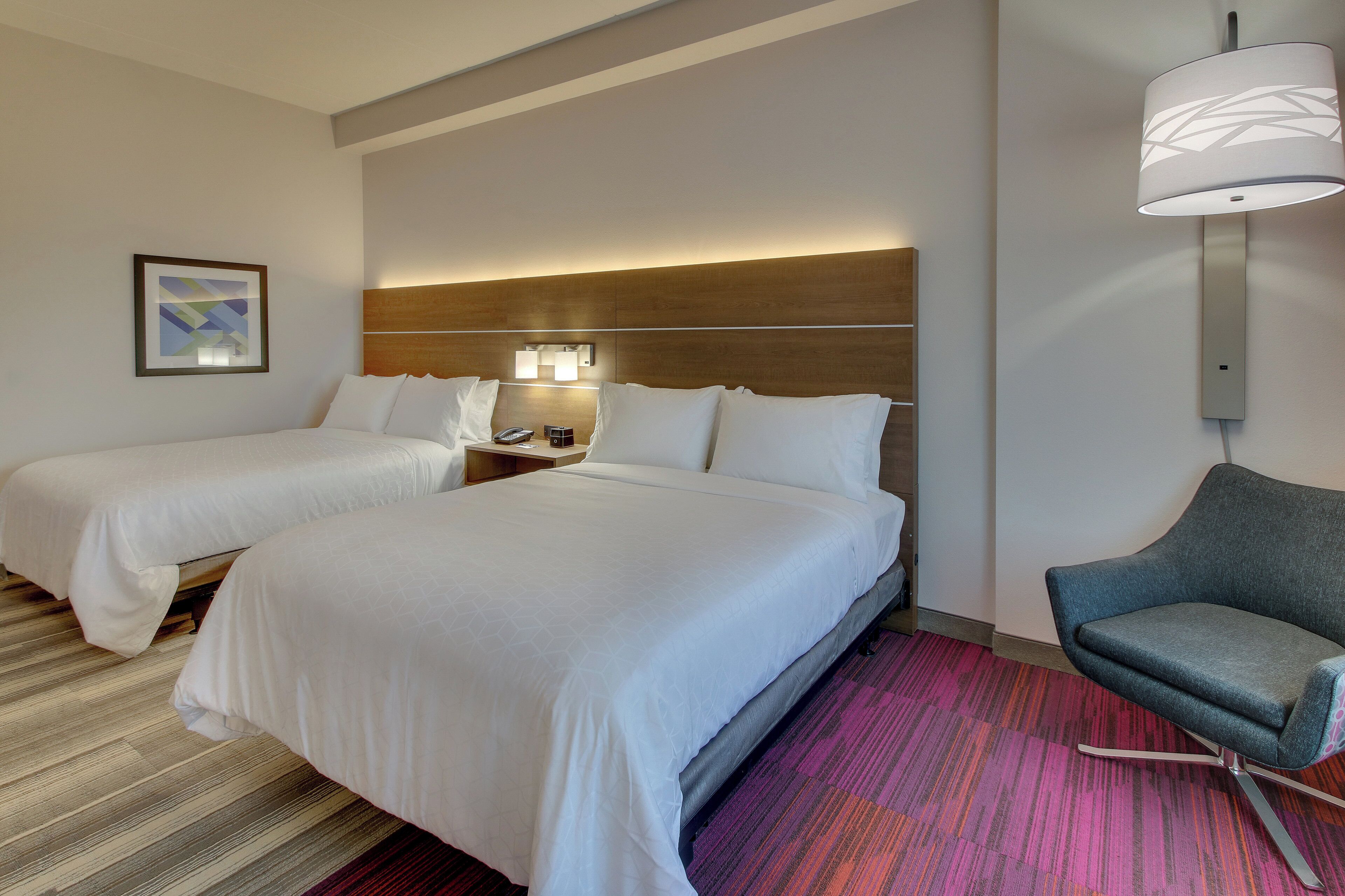 Habitación de hotel con dos camas, una mesita de noche, una lámpara, una silla y un cuadro en la pared.