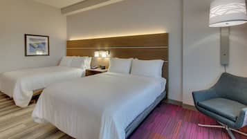 Habitación de hotel con dos camas, una mesita de noche, una lámpara, una silla y un cuadro en la pared.